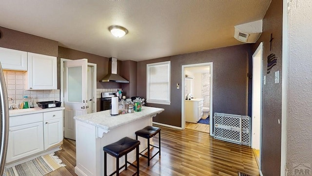 kitchen featuring white cabinetry, wall chimney range hood, wood finished floors, and backsplash