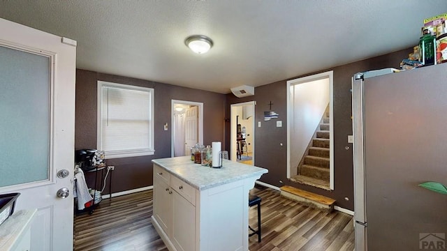 kitchen with a breakfast bar, wood finished floors, white cabinetry, freestanding refrigerator, and light countertops