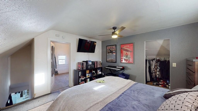 carpeted bedroom with ceiling fan, vaulted ceiling, a closet, a textured ceiling, and a textured wall