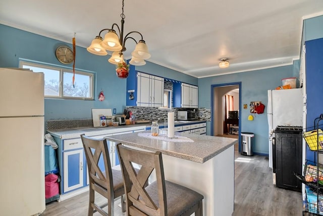 kitchen featuring arched walkways, light countertops, hanging light fixtures, and freestanding refrigerator