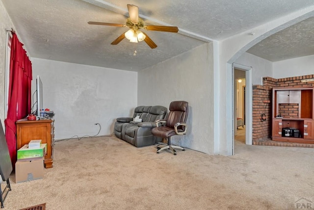 sitting room featuring arched walkways, a textured ceiling, a ceiling fan, and light colored carpet