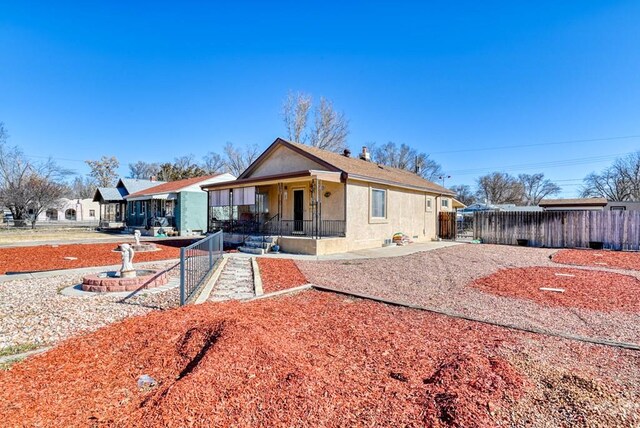 bungalow-style home with covered porch, fence, and stucco siding