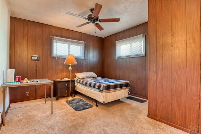 bedroom featuring a ceiling fan, light colored carpet, and wooden walls