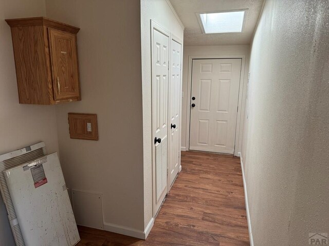 hallway featuring a skylight, baseboards, and wood finished floors