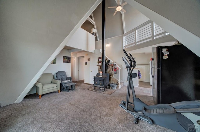 workout room featuring carpet flooring, a ceiling fan, a towering ceiling, and a wood stove