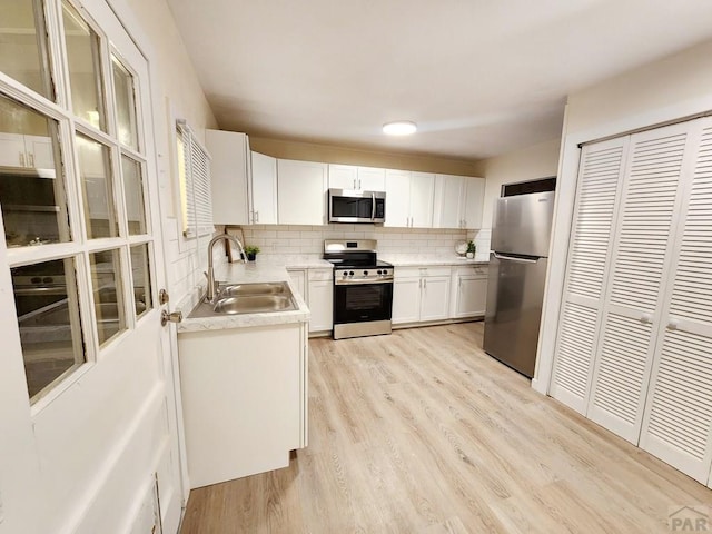 kitchen featuring stainless steel appliances, tasteful backsplash, light countertops, white cabinets, and a sink