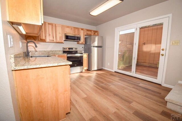 kitchen featuring light brown cabinets, a sink, baseboards, light wood-style floors, and appliances with stainless steel finishes