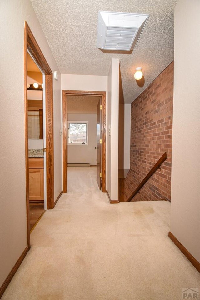 hallway featuring a textured ceiling, light carpet, an upstairs landing, baseboards, and baseboard heating