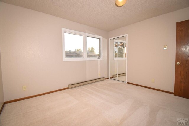 spare room with a baseboard radiator, baseboards, a textured ceiling, and light colored carpet