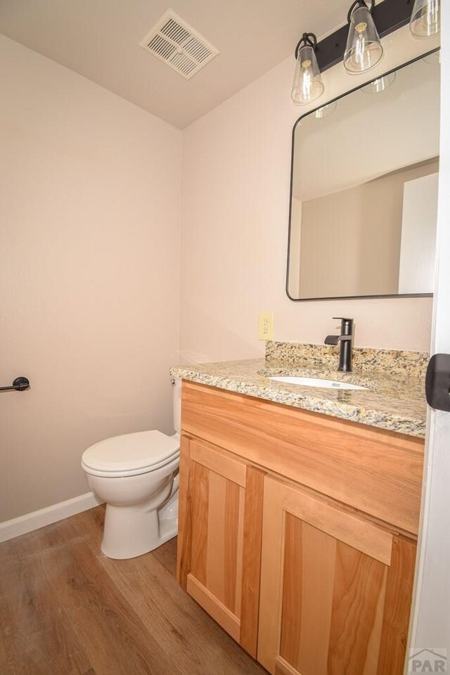 half bath with toilet, wood finished floors, vanity, visible vents, and baseboards