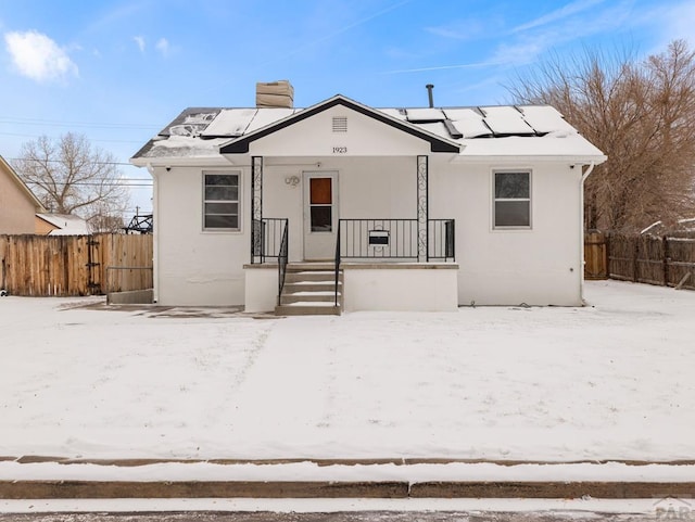 bungalow with solar panels, fence, stucco siding, covered porch, and a chimney