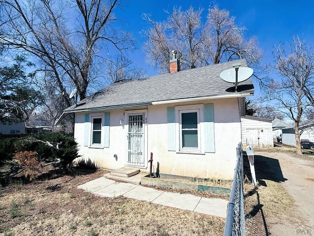 bungalow featuring a chimney, roof with shingles, and stucco siding