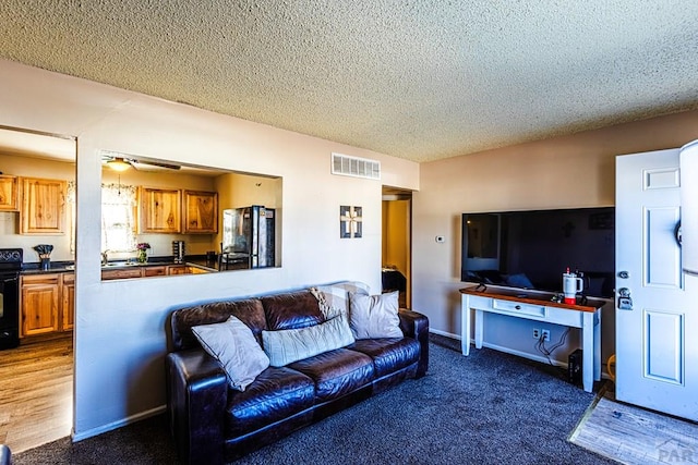 living room with a textured ceiling, visible vents, a ceiling fan, and dark carpet