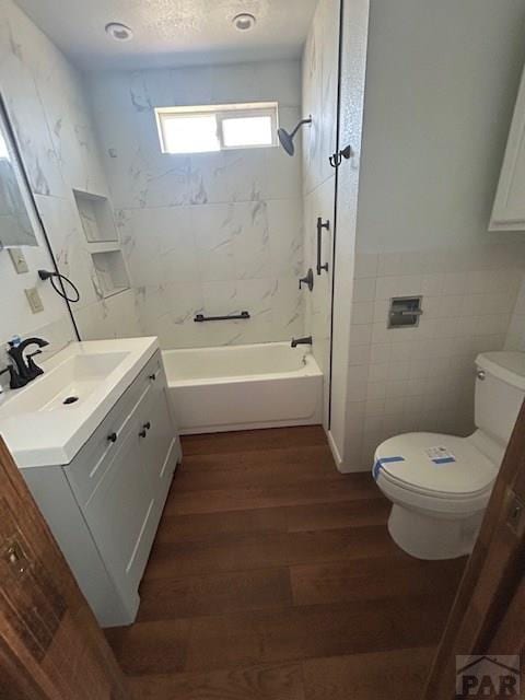 743 Vine Ave, Las Animas, CO 81054 - bathroom featuring vanity, tile walls, toilet, wood finished floors, and tub / shower combination