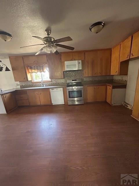 743 Vine Ave, Las Animas, CO 81054 - kitchen featuring white appliances, dark wood-type flooring, ceiling fan, tasteful backsplash, and brown cabinetry
