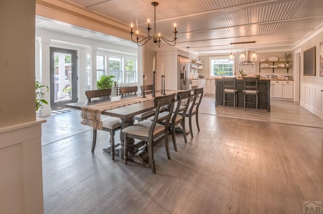 dining space featuring a wainscoted wall, a decorative wall, a chandelier, and light wood-style floors