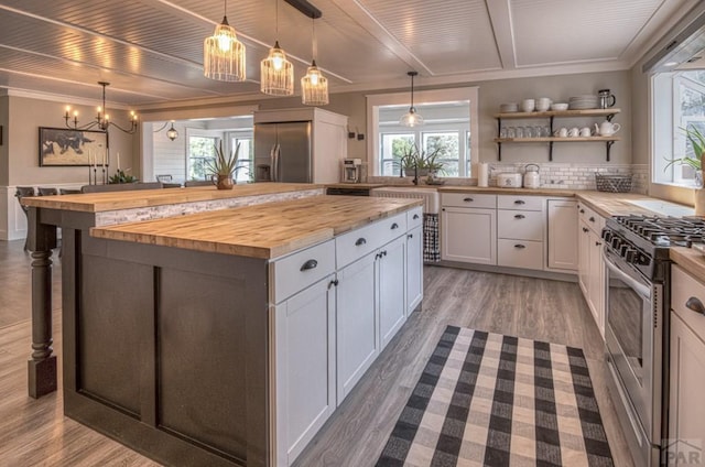 kitchen with crown molding, wood counters, wood finished floors, appliances with stainless steel finishes, and an inviting chandelier