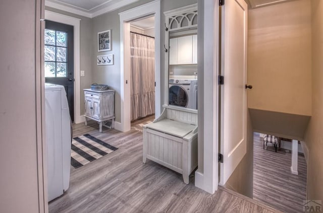clothes washing area featuring baseboards, ornamental molding, wood finished floors, washer and dryer, and cabinet space
