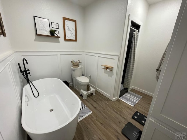 bathroom with a wainscoted wall, a soaking tub, a decorative wall, toilet, and wood finished floors