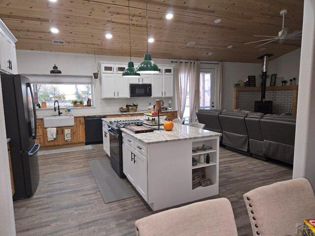 kitchen featuring glass insert cabinets, a wood stove, hanging light fixtures, black appliances, and white cabinetry