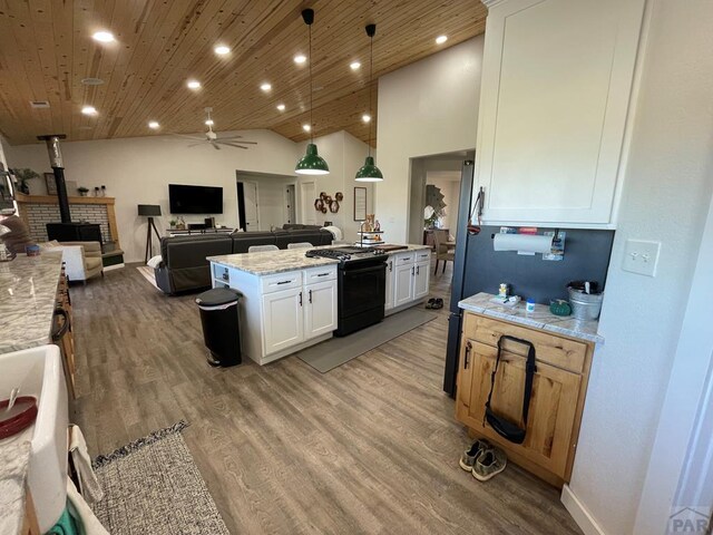 kitchen featuring a center island, hanging light fixtures, a wood stove, white cabinetry, and light stone countertops