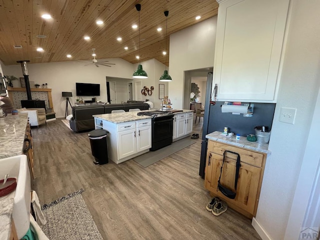 kitchen featuring a center island, hanging light fixtures, a wood stove, white cabinetry, and light stone countertops