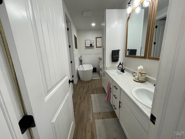 full bathroom featuring double vanity, a freestanding tub, a sink, and wood finished floors