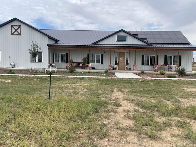 view of front of property with a porch, metal roof, roof mounted solar panels, a front lawn, and board and batten siding