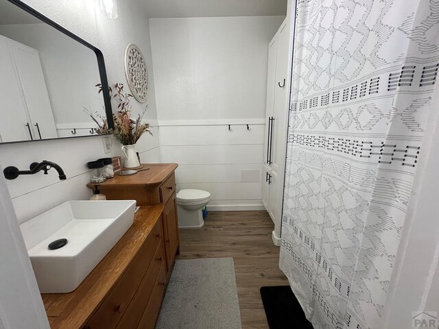 full bath with toilet, a shower with shower curtain, wood finished floors, and vanity