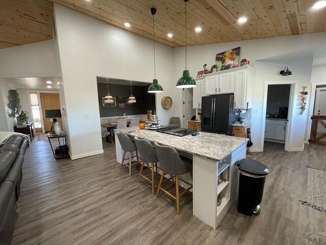 kitchen with light stone counters, black fridge with ice dispenser, white cabinetry, open floor plan, and decorative light fixtures