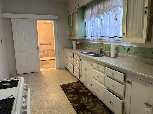 kitchen featuring light floors, gas range oven, light countertops, white cabinets, and a sink