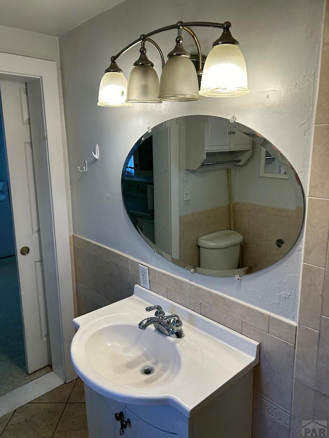 bathroom with toilet, a wainscoted wall, vanity, tile walls, and tile patterned floors