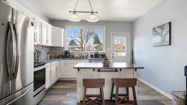 kitchen featuring dark wood-style floors, stainless steel appliances, hanging light fixtures, white cabinets, and a kitchen breakfast bar