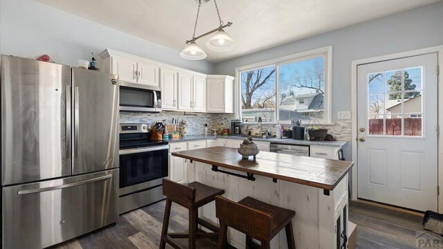 kitchen with dark wood-style floors, stainless steel appliances, hanging light fixtures, decorative backsplash, and white cabinets