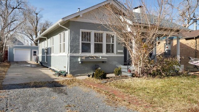 view of side of home featuring a garage, an outdoor structure, concrete driveway, stucco siding, and a chimney