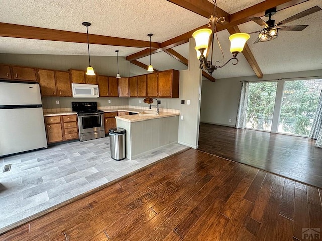 kitchen with white microwave, brown cabinetry, freestanding refrigerator, open floor plan, and stainless steel range with electric stovetop