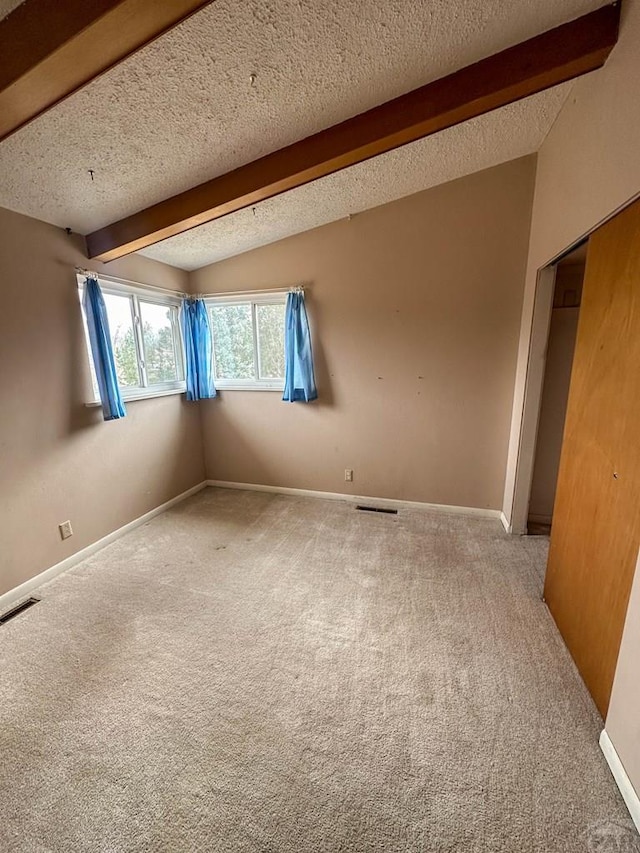 empty room with vaulted ceiling with beams, a textured ceiling, carpet, and visible vents