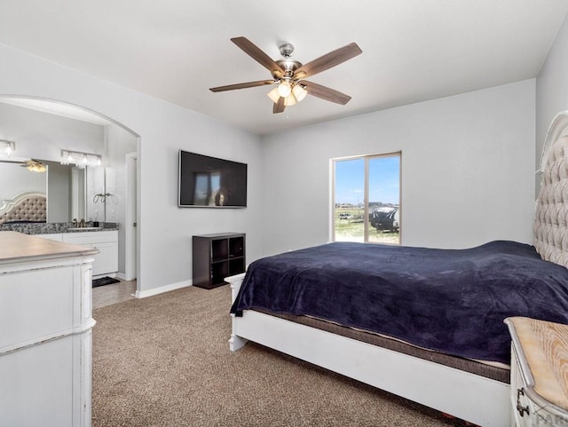 bedroom featuring baseboards, ensuite bathroom, a ceiling fan, arched walkways, and light colored carpet