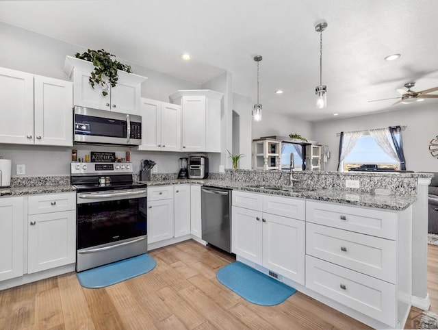 kitchen featuring a sink, appliances with stainless steel finishes, a peninsula, white cabinetry, and light wood-style flooring