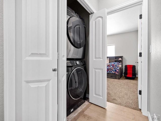 laundry area featuring laundry area, stacked washer and clothes dryer, light colored carpet, and light wood-type flooring