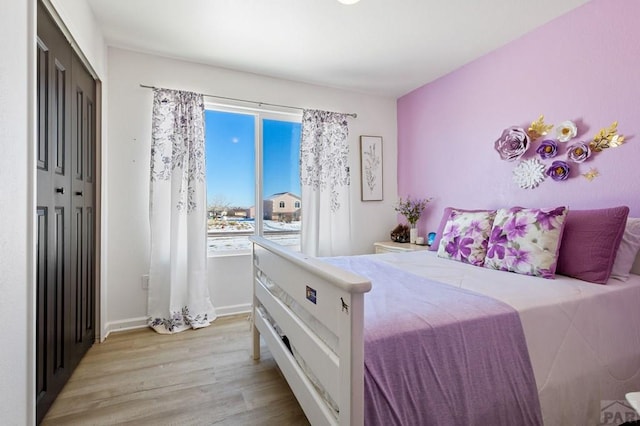 bedroom with a closet, light wood-type flooring, and baseboards