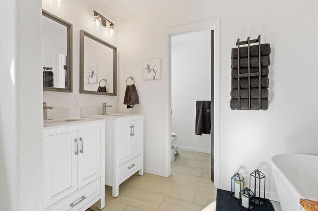 full bathroom with a soaking tub, two vanities, a sink, and toilet