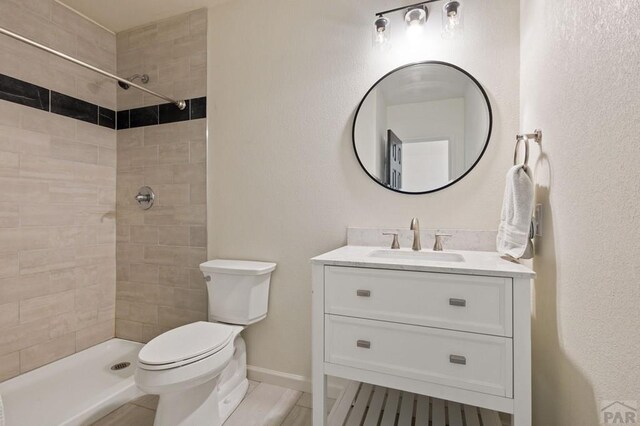 full bath with vanity, a tile shower, toilet, and baseboards