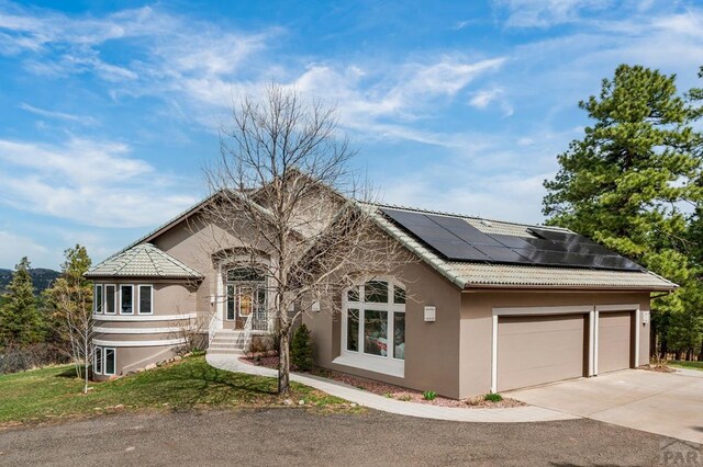 view of front facade featuring a tiled roof, roof mounted solar panels, an attached garage, stucco siding, and driveway