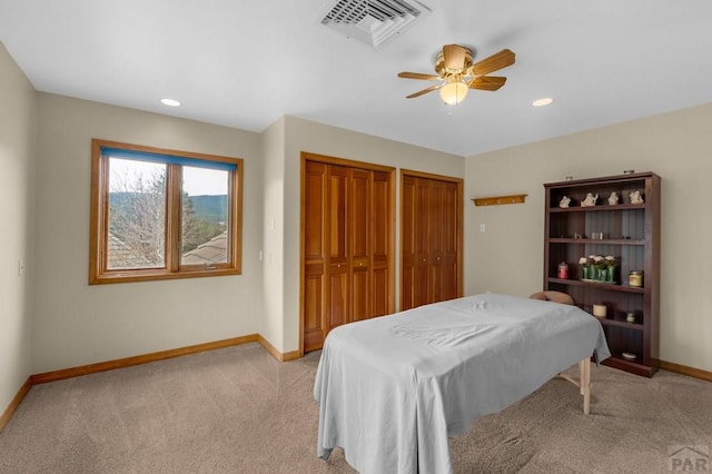 bedroom featuring light colored carpet, visible vents, two closets, and baseboards