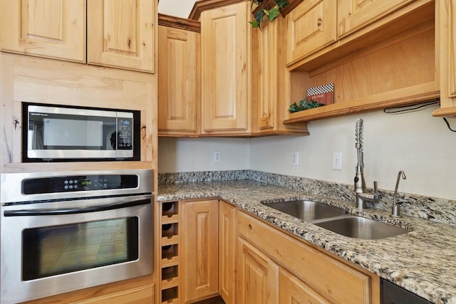 kitchen with light stone counters, appliances with stainless steel finishes, light brown cabinets, open shelves, and a sink