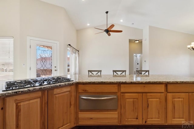 kitchen with brown cabinets, a warming drawer, stainless steel gas stovetop, vaulted ceiling, and ceiling fan with notable chandelier