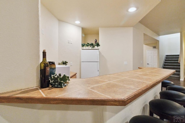 kitchen with a breakfast bar area, freestanding refrigerator, and recessed lighting