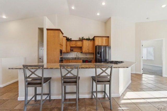 kitchen featuring dark stone countertops, stainless steel refrigerator with ice dispenser, brown cabinets, and a kitchen breakfast bar