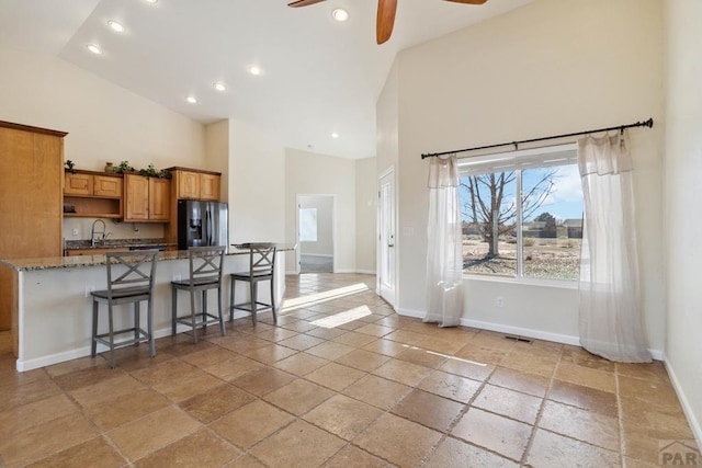 kitchen featuring brown cabinetry, a kitchen breakfast bar, high vaulted ceiling, and stainless steel fridge with ice dispenser